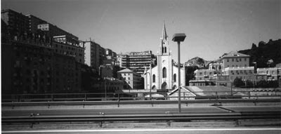 fotografia in bianco e nero di uno scorcio di Genova: in primo piano un viale che taglia la città e in secondo piano una chiesa (fonte: Emanuele Piccardo)