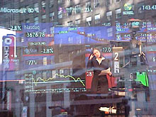 fotografia a colori del Nasdaq: attraverso un vetro si vede lo studio televisivo e l'annunciatrice di fronte alle telecamere commentare l'andamento della borsa; sul riflesso del vetro i palazzi di fronte a Times Square (autore: Gianluigi D'Angelo)